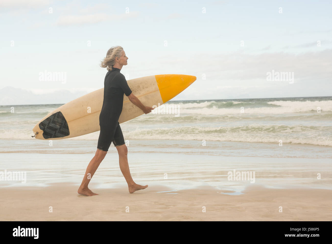 Side view of woman walking with surfboard on shore against sky at beach Stock Photo