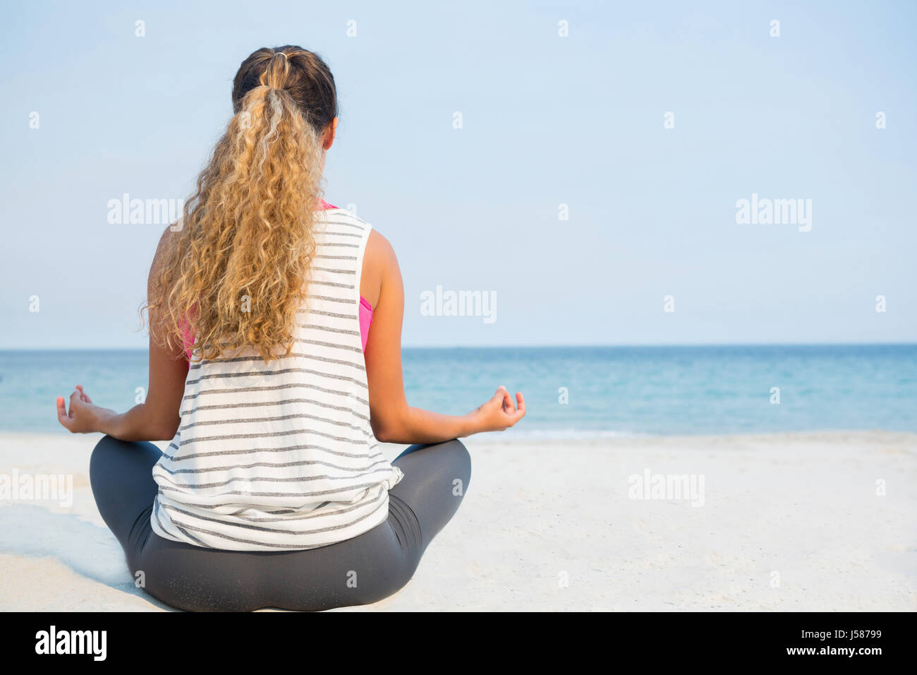 Rear view of woman practicing yoga at beach against clear blue sky on ...