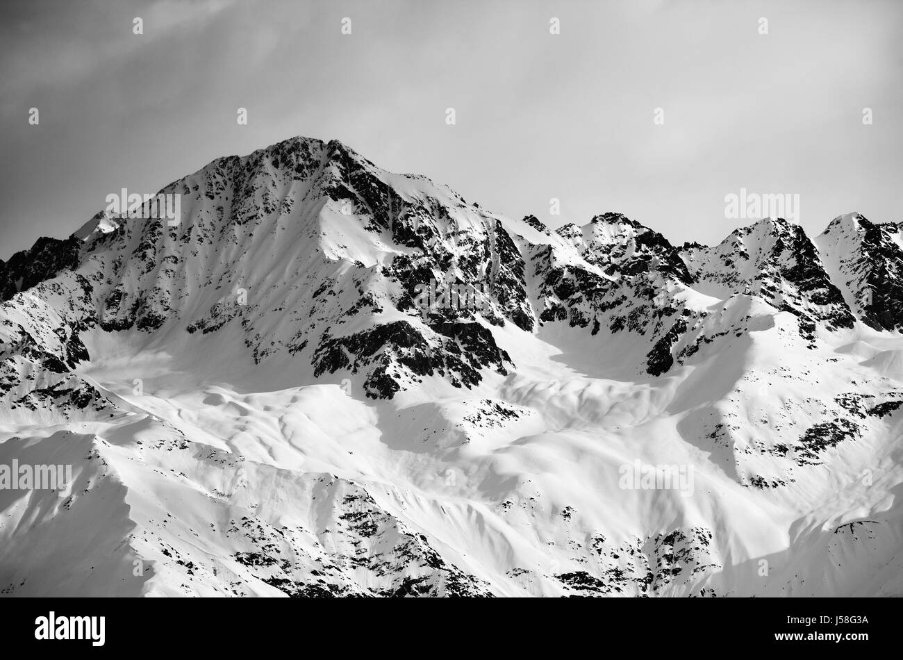 Black and white view on snow sunlight mountain and gray sky in evening. Caucasus Mountains. Svaneti region of Georgia. Stock Photo