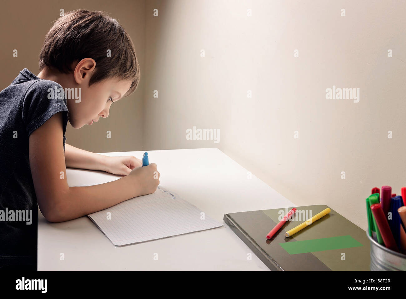 Boy sitting at the desk home and doing his homework. Child writting. School, children, education concept Stock Photo