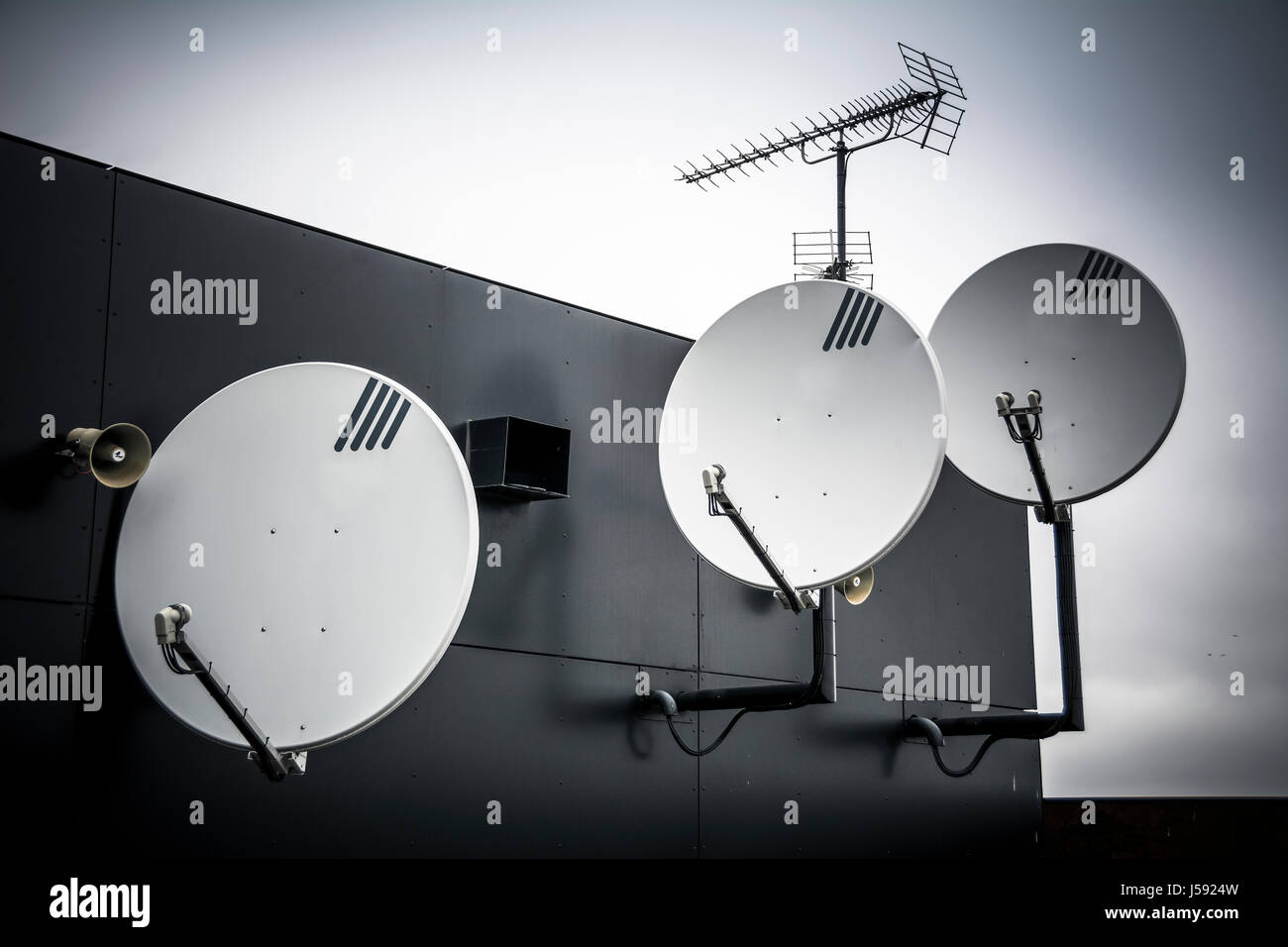 Trio of satellite dishes attached to high wall on building Stock Photo