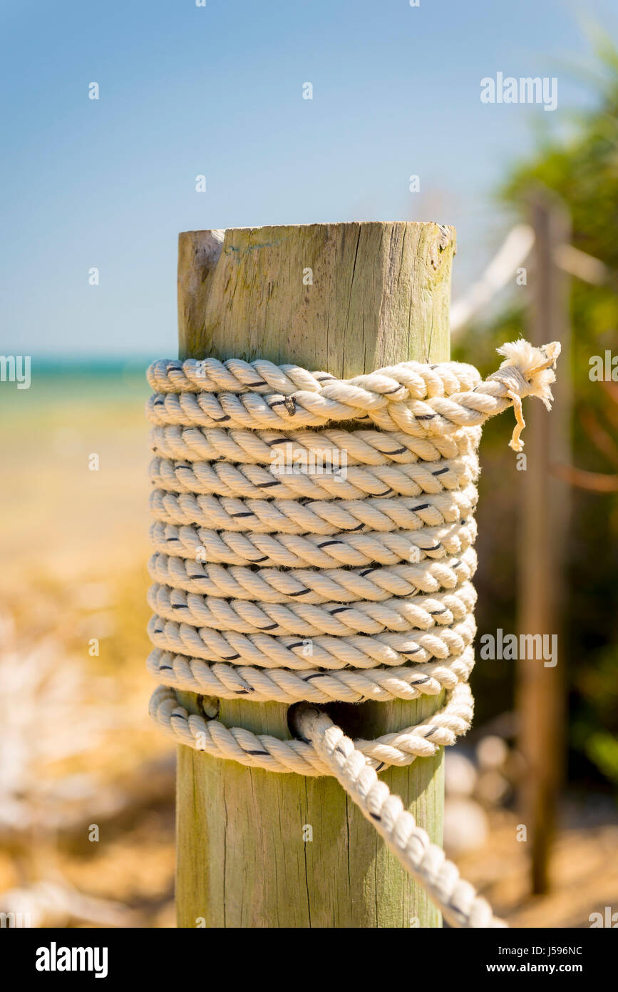 Marine rope tied to a wooden pole beside the ocean Stock Photo
