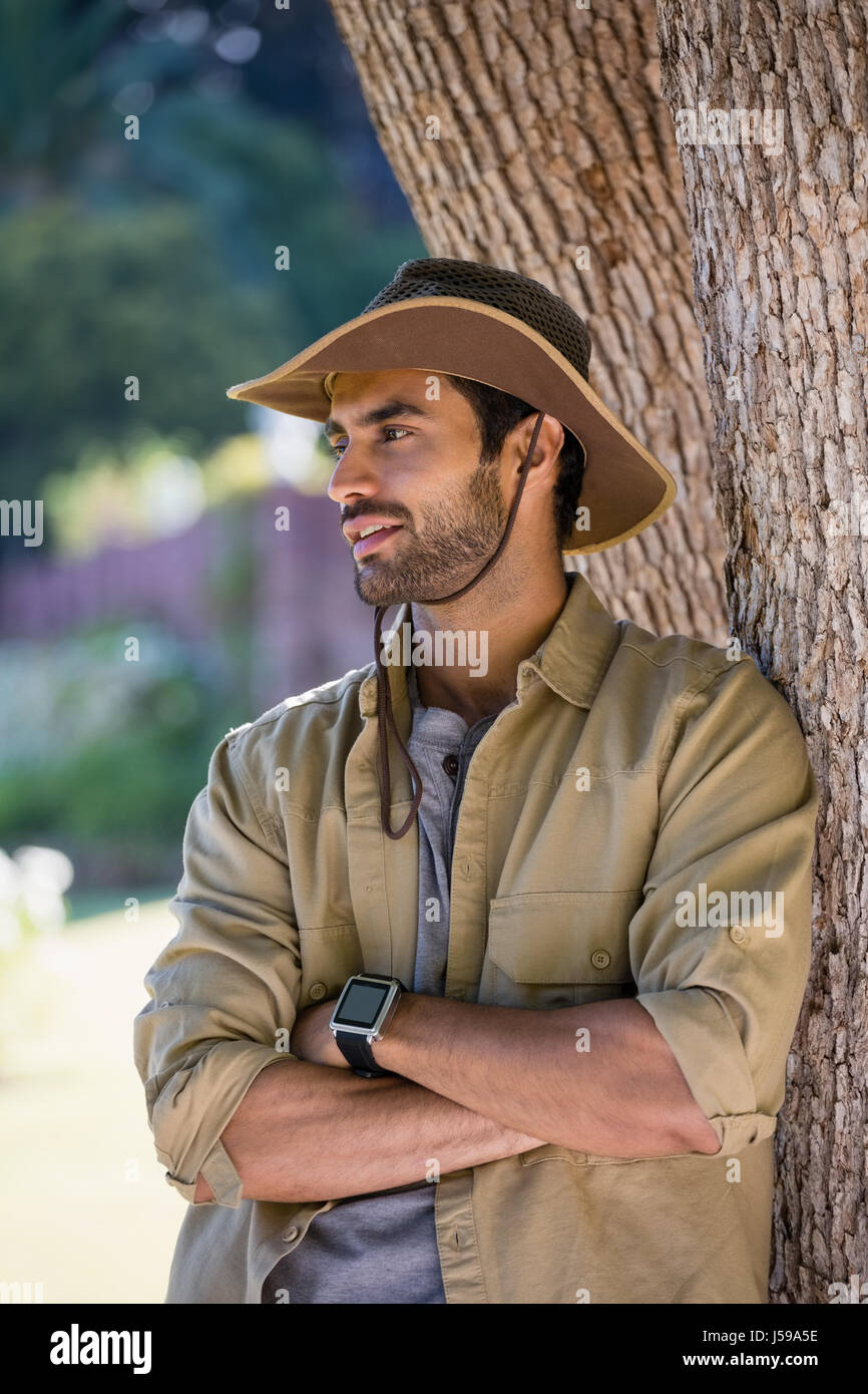 Smiling man standing with arms crossed near tree trunk in forest Stock Photo