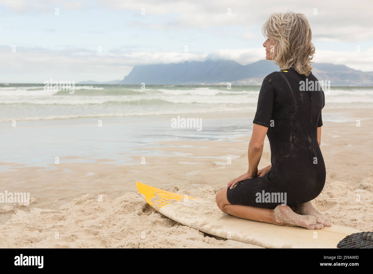 Close up of woman kneeling on surfboard against cloudy sky Stock Photo