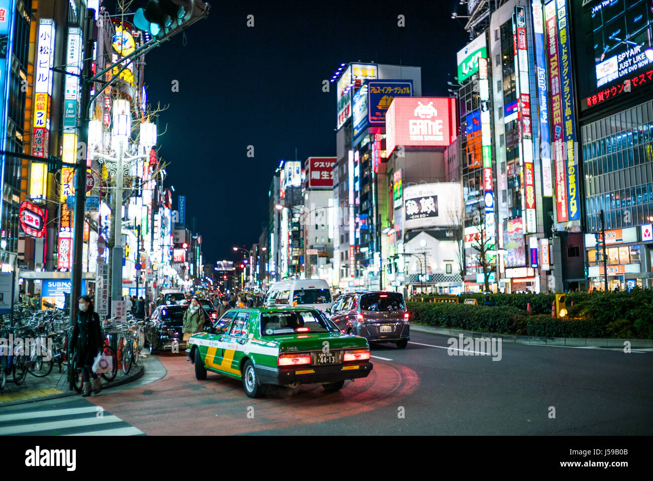 A taxi pulls up to the kerb one night in the vibrantly illuminated district of Akihabara, Tokyo, Japan Stock Photo