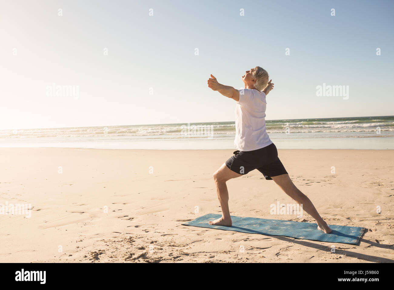 Active senior man practicing yoga at beach Stock Photo