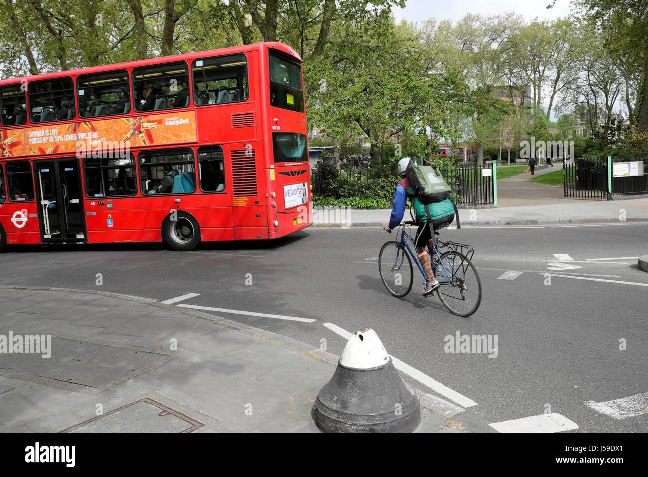 Male cyclist riding his bike, wearing rucksack and lycra cycling behind a double decker bus near the park Newington Green London N5 UK  KATHY DEWITT Stock Photo
