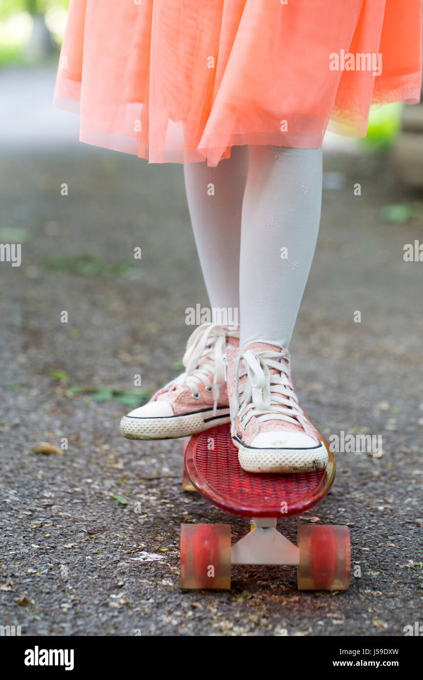 Close up little girl in a skirt riding a skateboard ride in the park