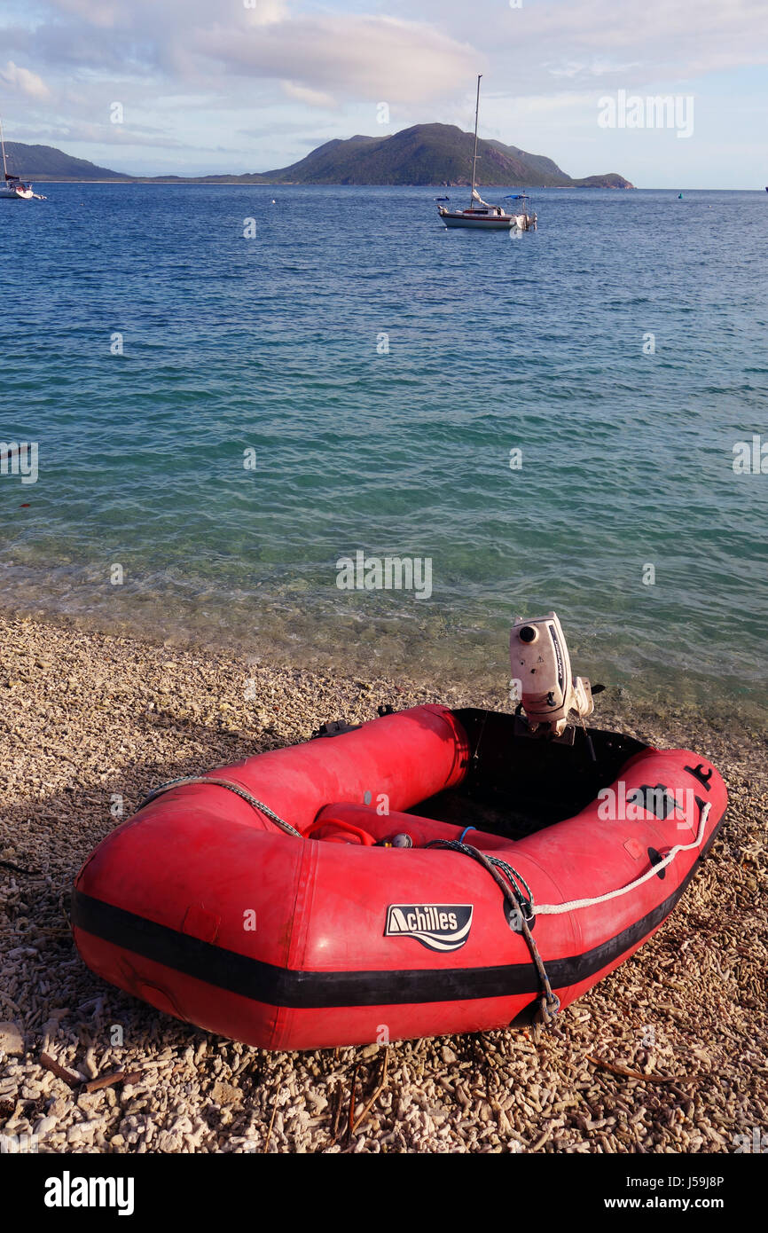 Small red inflatable boat on coral rubble beach with yachts moored in background, Fitzroy Island, Great Barrier Reef, Queensland, Australia. No PR Stock Photo