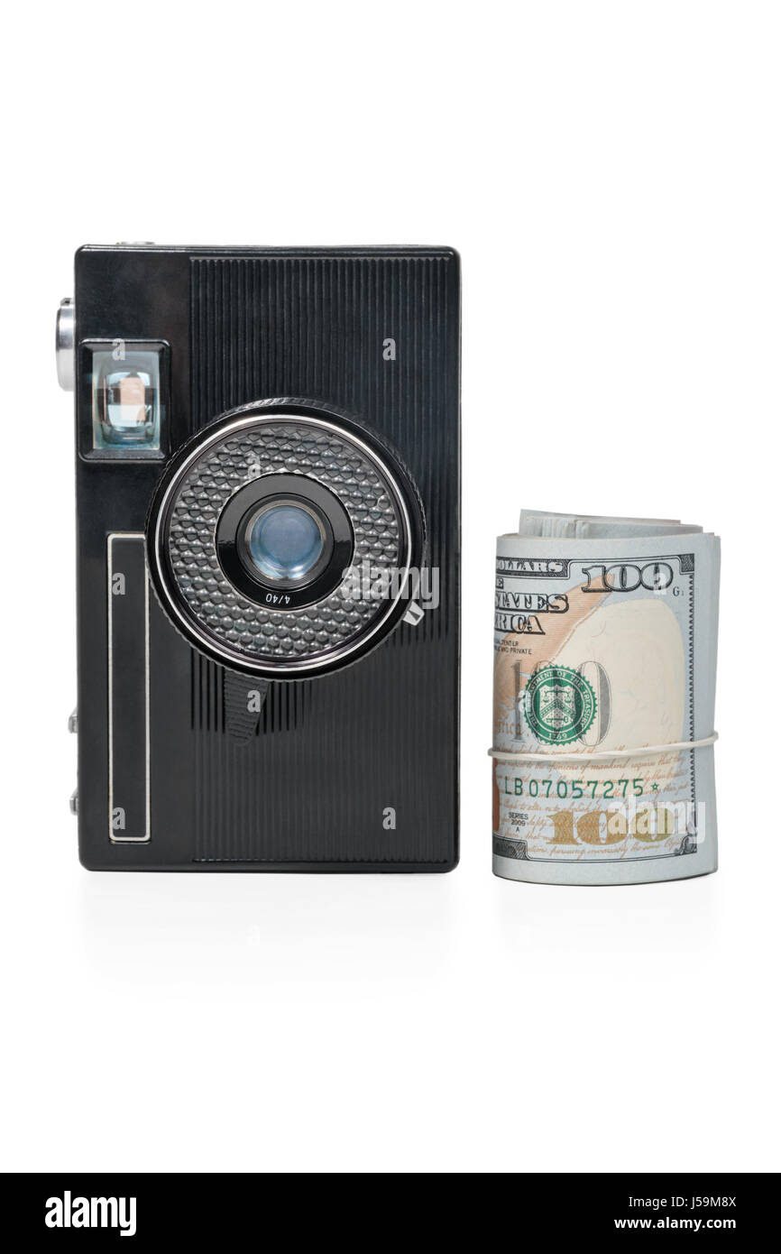 Old retro camera in vertical position and a bundle of money rolled up in a tube isolated on a white background Stock Photo