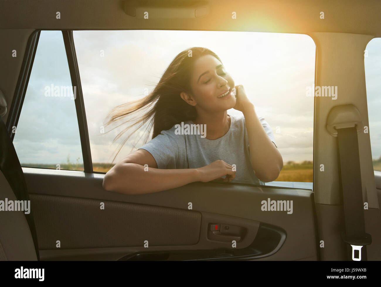 Young woman with windblown hair enjoying sun outside of car Stock Photo