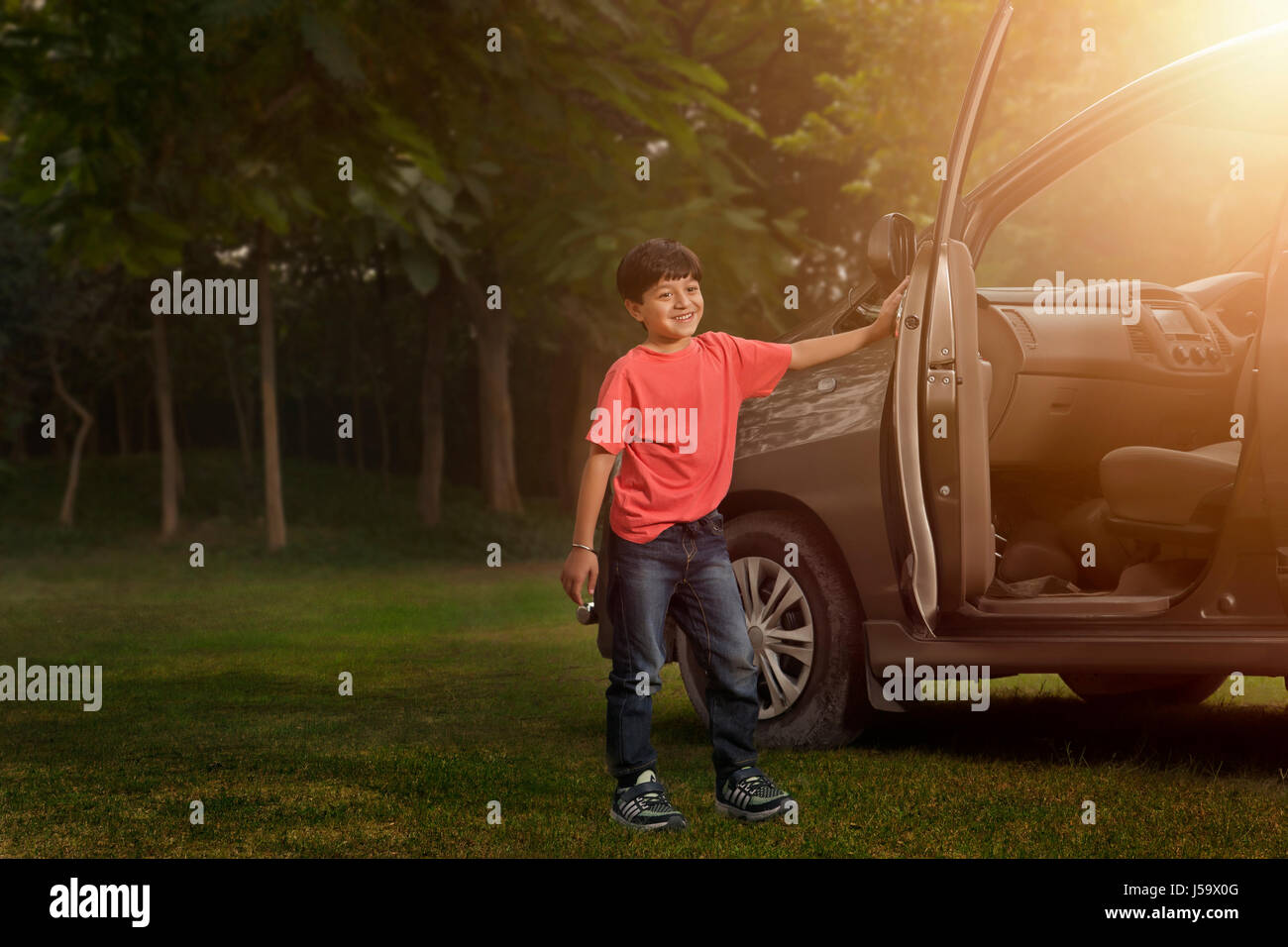 Boy standing near car door in park Stock Photo