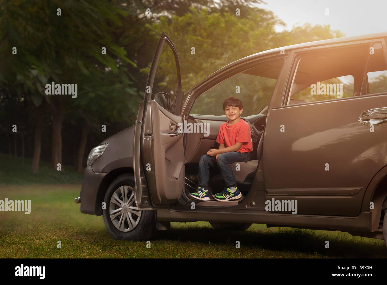 Boy sitting on car front seat in park Stock Photo