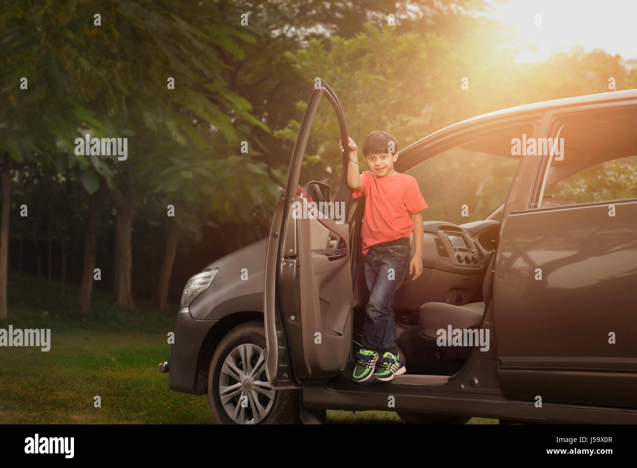 Boy standing in car doorway In park Stock Photo