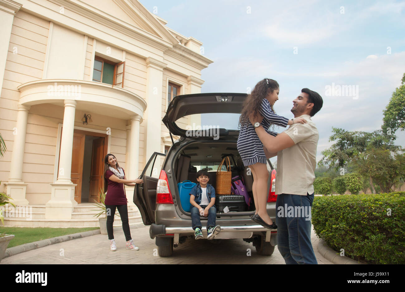 Family standing outdoors by car father lifting daughter Stock Photo