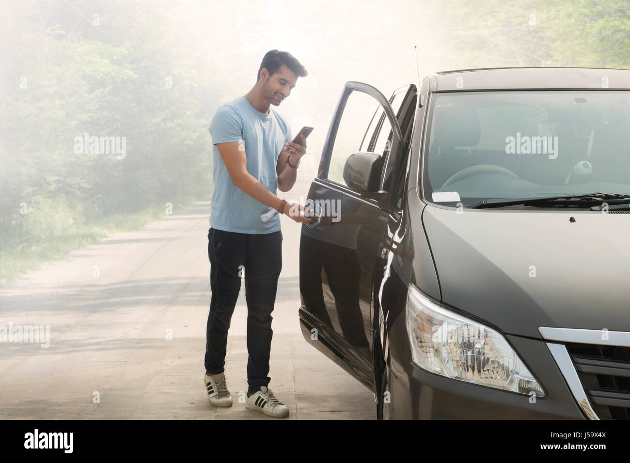 Young man with phone opening black car door Stock Photo Alamy