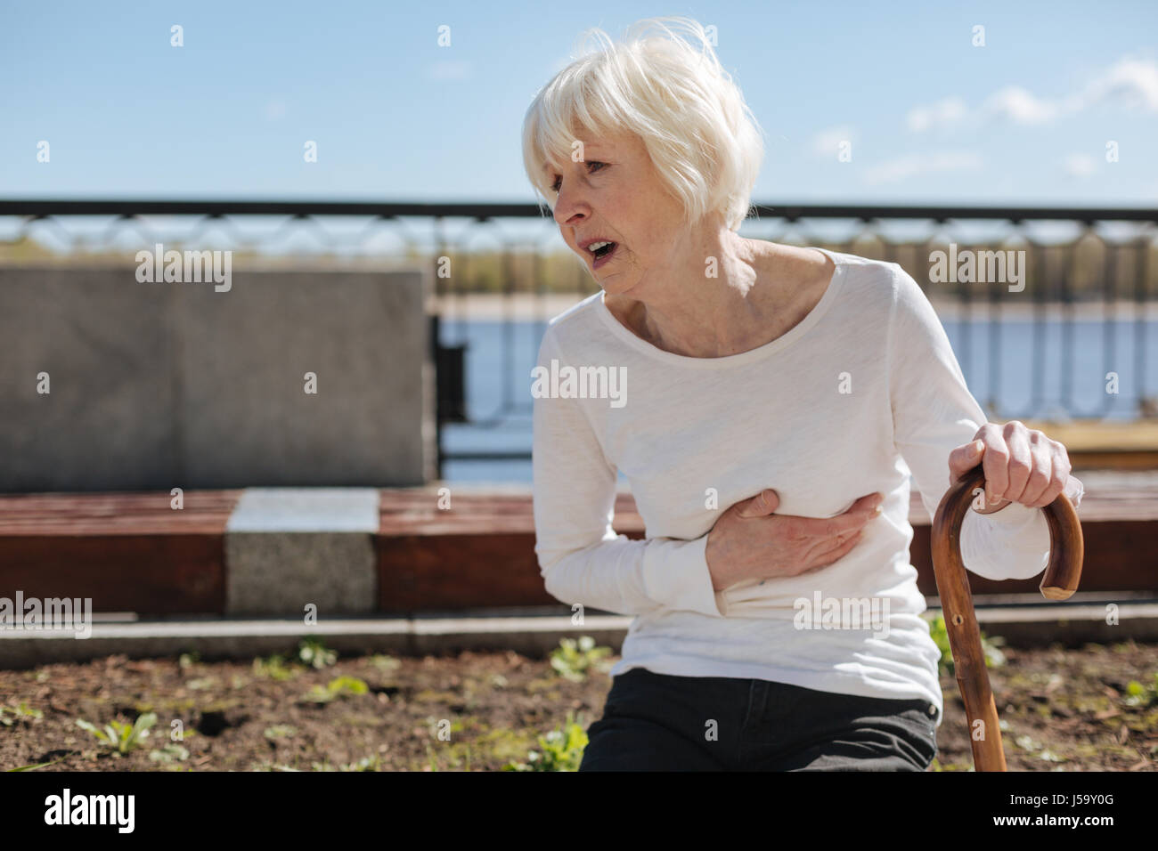 Unhappy woman enduring heart attack near the river Stock Photo