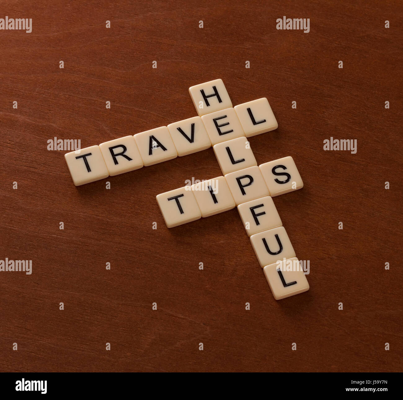 Crossword puzzle with words Helpful Travel Tips. World travel concept. Ivory tiles with capital letters on mahogany board. Stock Photo