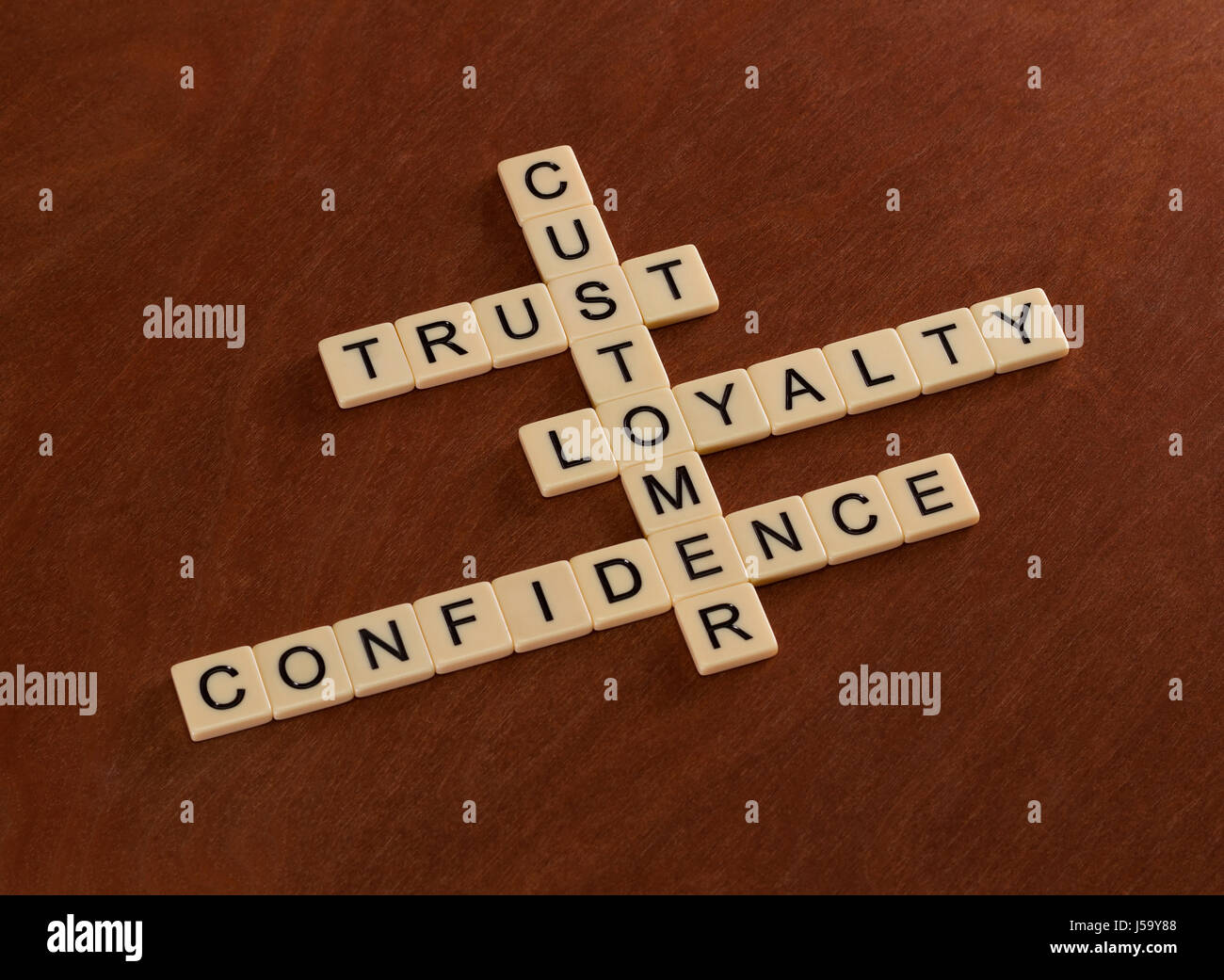 Crossword puzzle with words Trust, Loyalty, Confidence. Customer loyalty concept. Ivory tiles with capital letters on mahogany board. Stock Photo