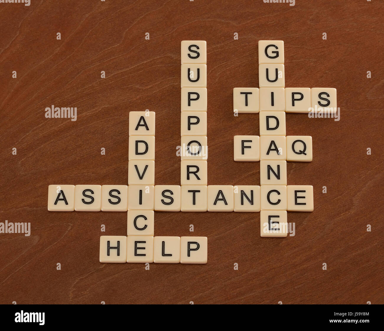 Crossword puzzle with words Support, Help, FAQ, Assistance. Customer care concept. Ivory tiles with capital letters on mahogany board. Stock Photo