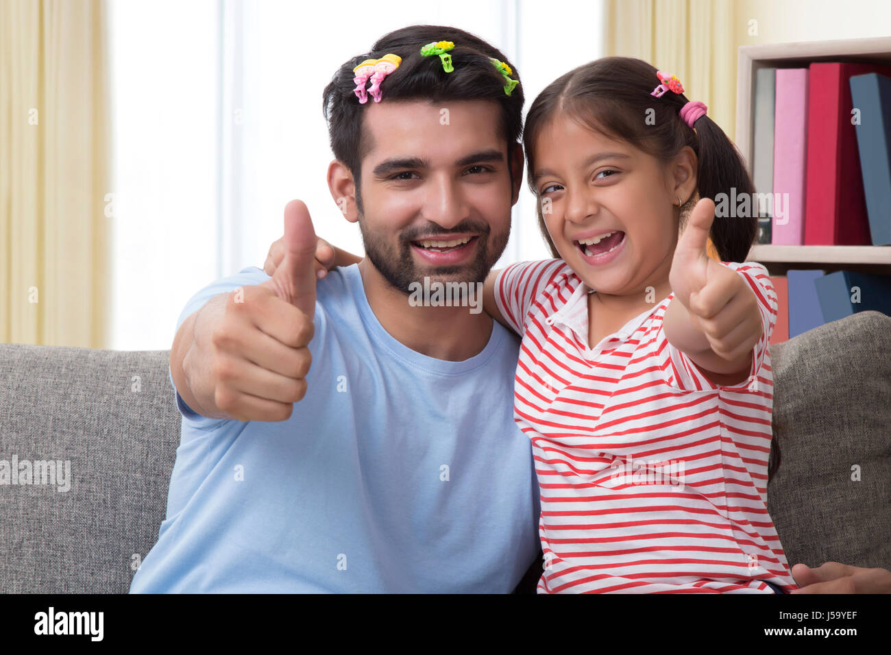 Funny father wearing hair clips and daughter making thumbs up sign Stock Photo