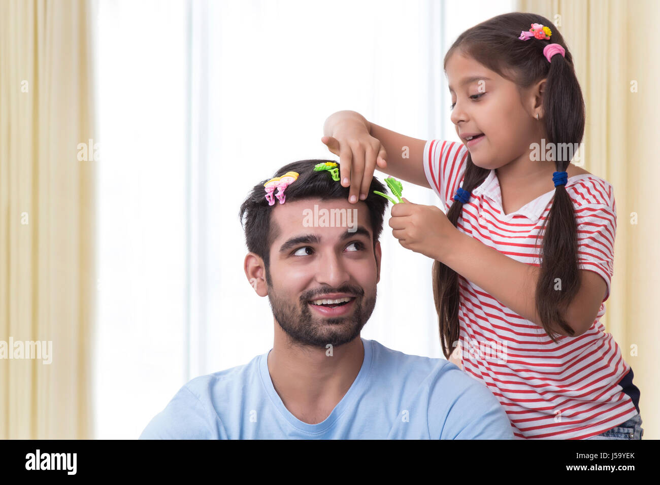Daughter placing clips in fathers hair and making funny hair style Stock Photo