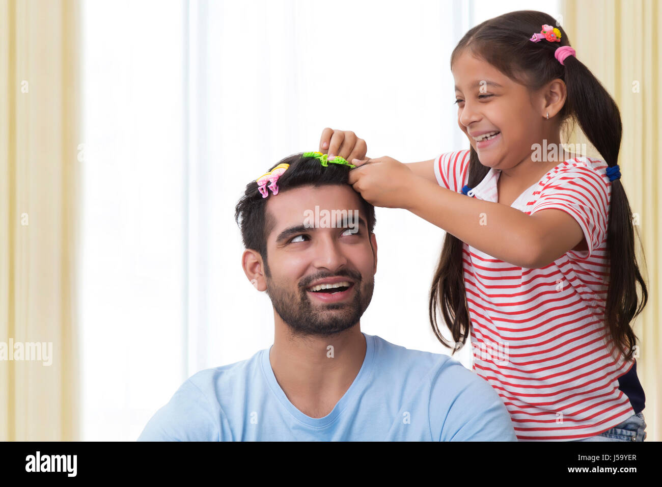 Daughter placing clips in fathers hair and making funny hair style Stock Photo