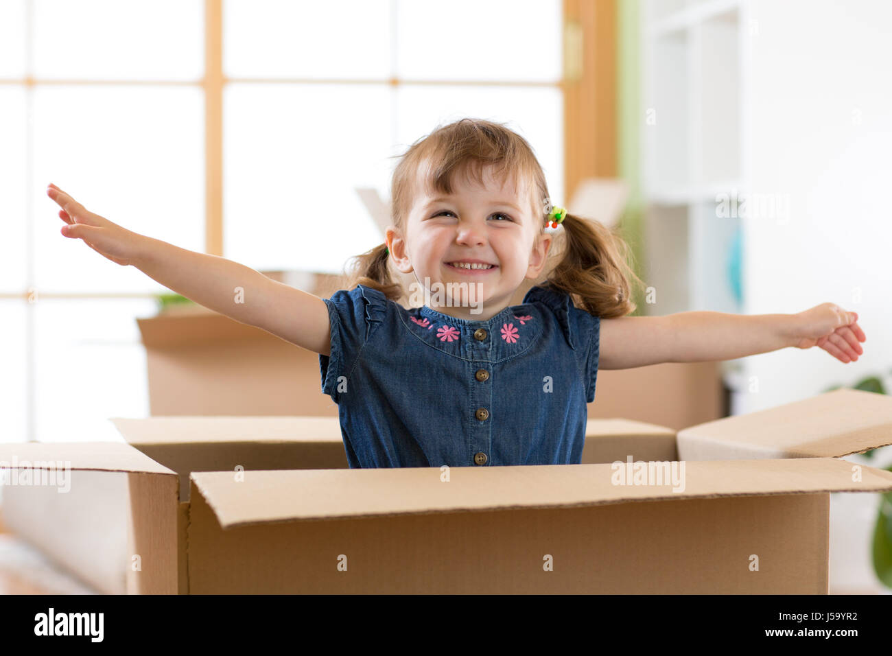 Laughing child girl sitting inside cardboard boxe in her new home Stock Photo