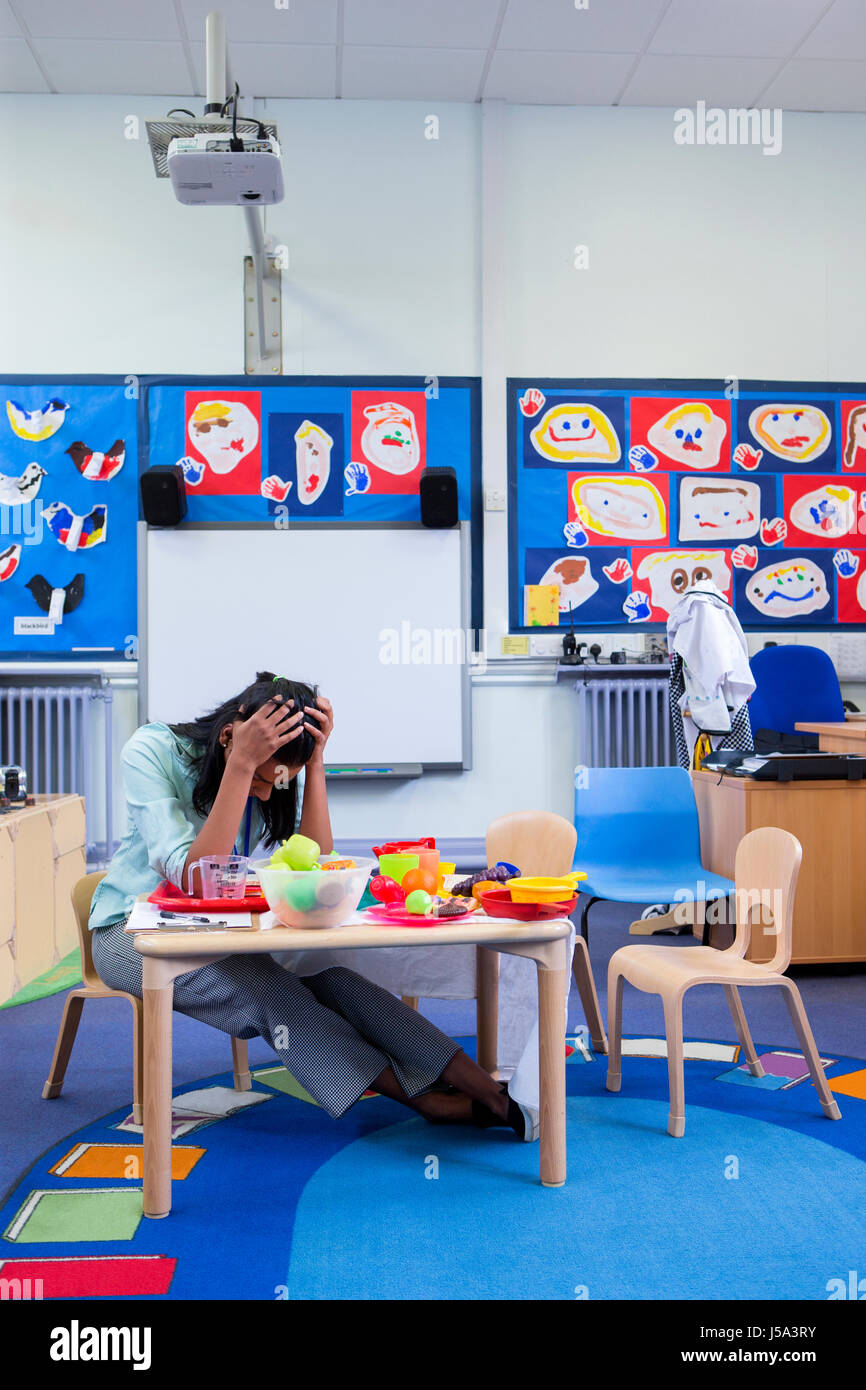 Stressed nursery teacher in a classroom. She has her head in her hands