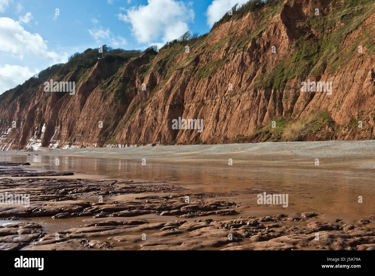 view along the empty beach with the red cliffs of Peak Hill in the background on Sidmouth seafront in Devon, England, on the Jurassic Coast. Stock Photo