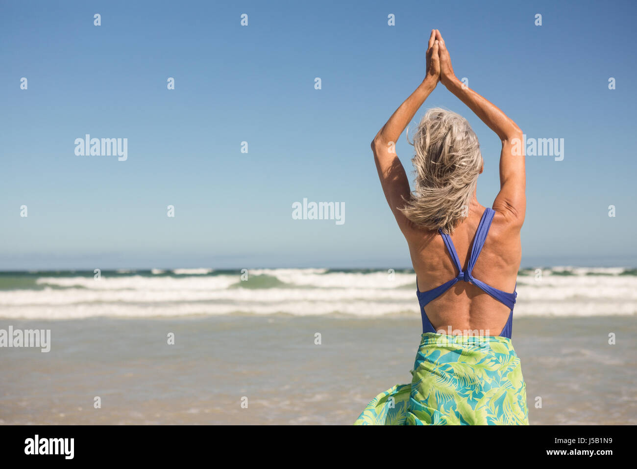 Rear view of woman practising yoga while standing at beach Stock Photo ...