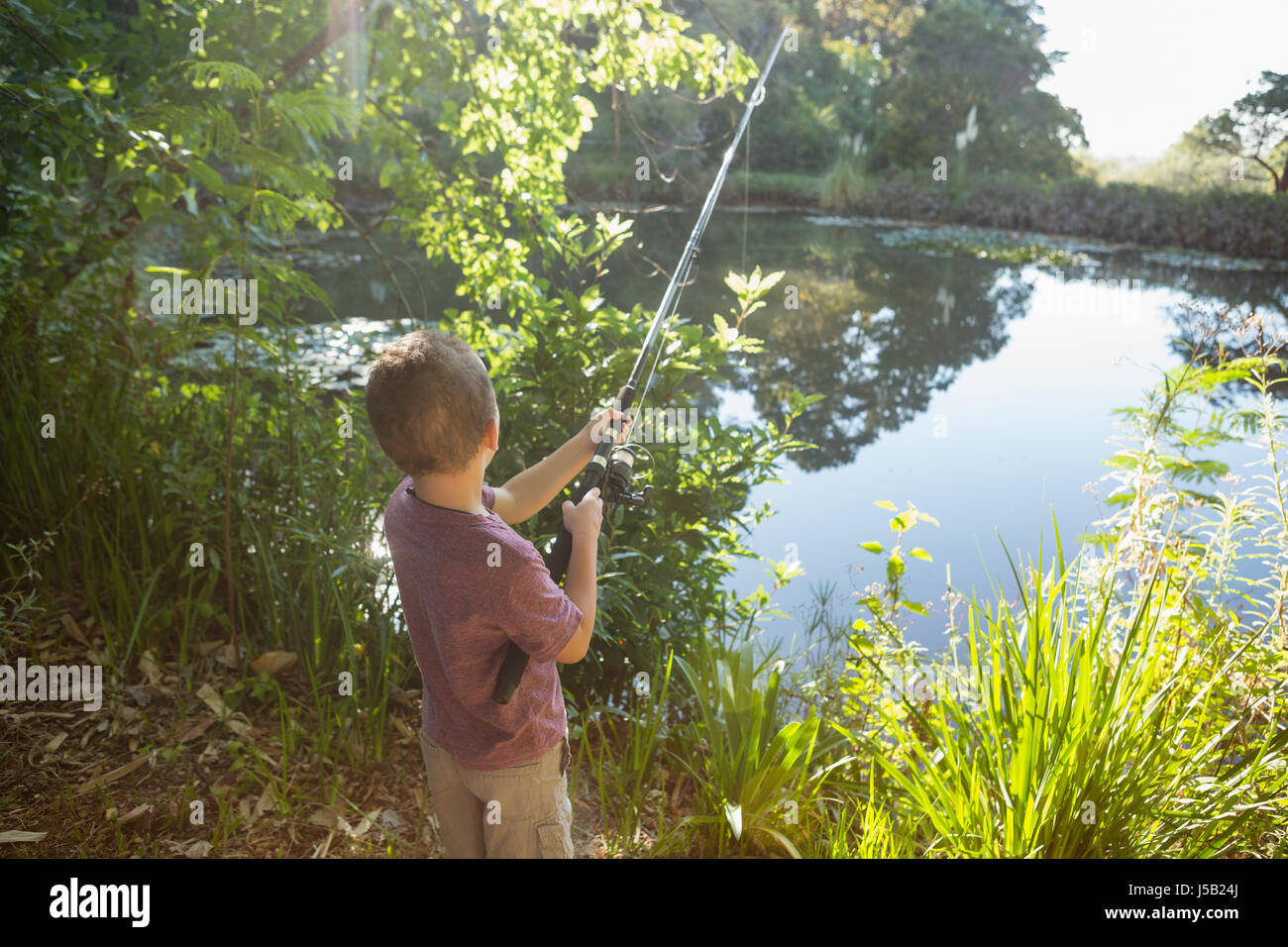 Side view of teenage boy fishing with rod in lake while standing against  cloudy sky stock photo