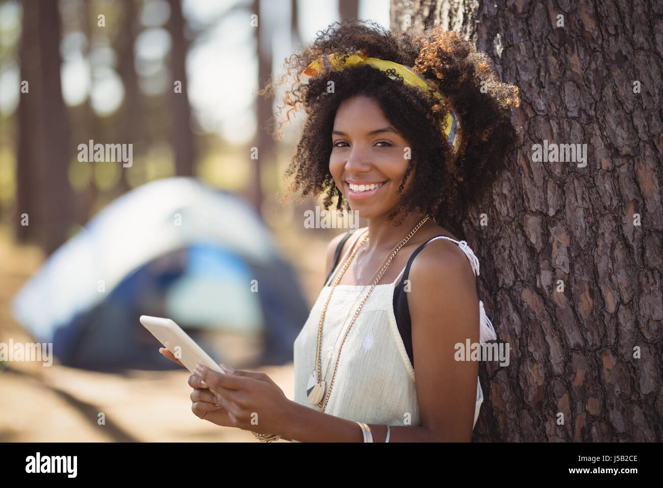 Portrait of happy girl using smart phone while standing by tree against tent Stock Photo