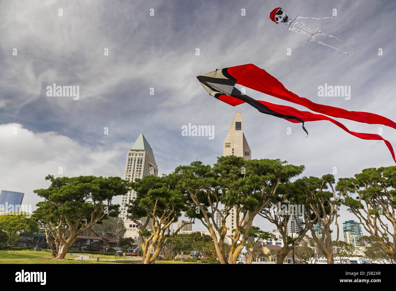 Windy Day Kite Flying in Seaport Village near San Diego California Harbor with Manzanita Trees and Urban Highrise City Center Buildings on Skyline Stock Photo
