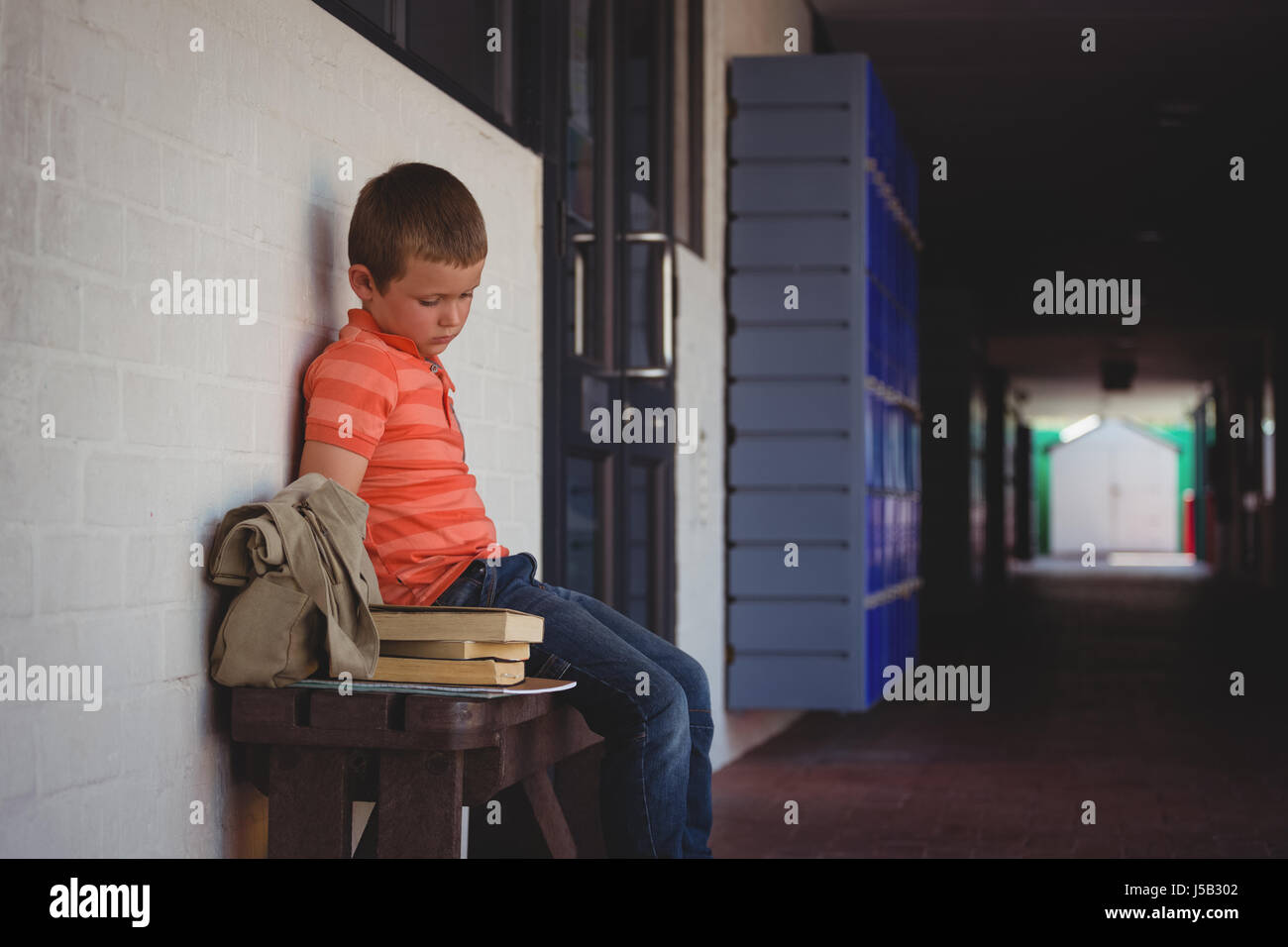 Sad boy sitting on bench by wall in corridor at school Stock Photo - Alamy
