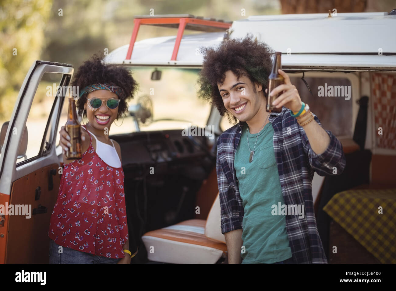Portrait of cheerful friends holding beer bottles while standing by van Stock Photo
