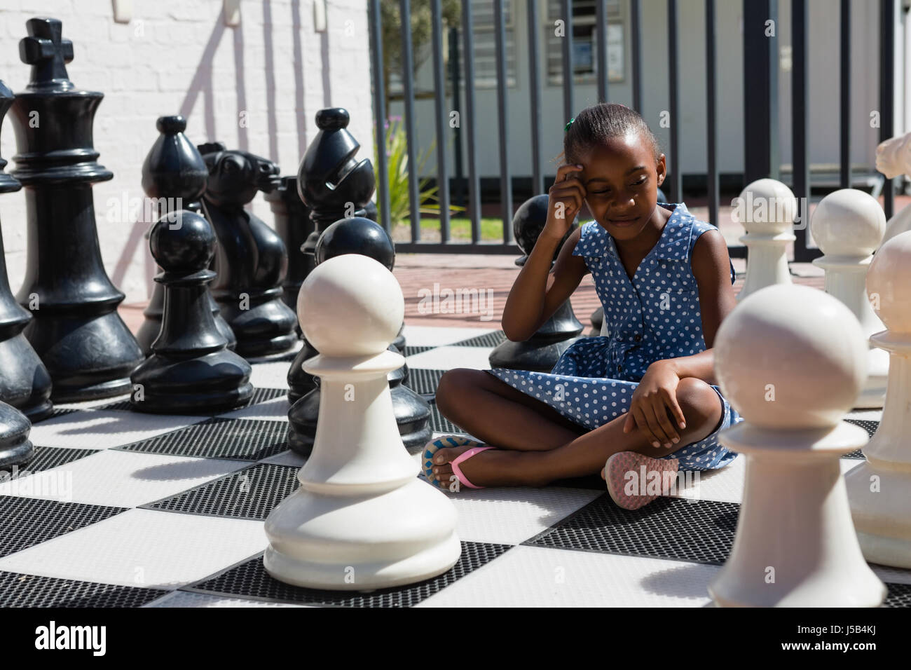 Thoughtful girl sitting by chess pieces on sunny day Stock Photo
