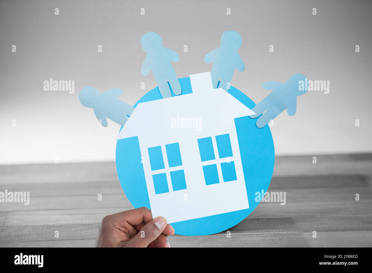 hand holding a house in paper against blue paper cut out figures on globe Stock Photo
