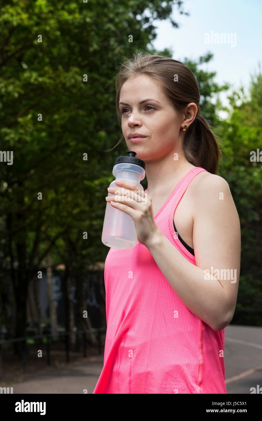 Athletic woman drinking water, while training outdoors in a natural setting. Action and healthy lifestyle concept. Stock Photo