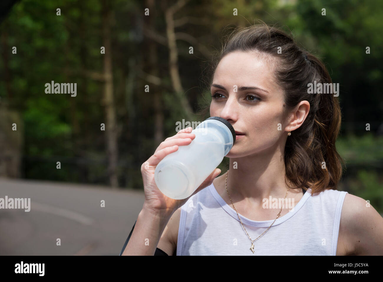 Athletic woman drinking water, while training outdoors in a natural setting. Action and healthy lifestyle concept. Stock Photo