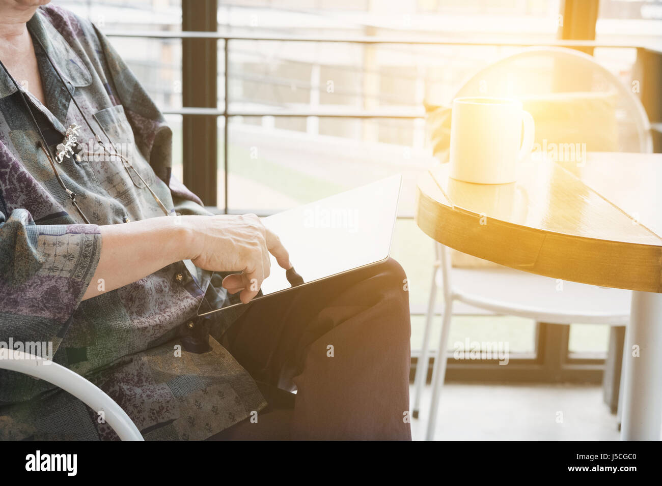 asian senior woman sitting and resting in cafe coffee shop near window using digital tablet computer. social networking concept Stock Photo