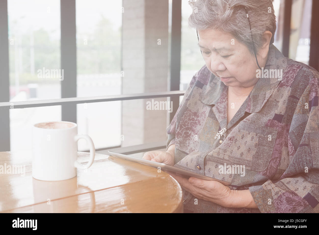asian senior woman sitting and resting in cafe coffee shop near window using digital tablet computer. social networking concept Stock Photo
