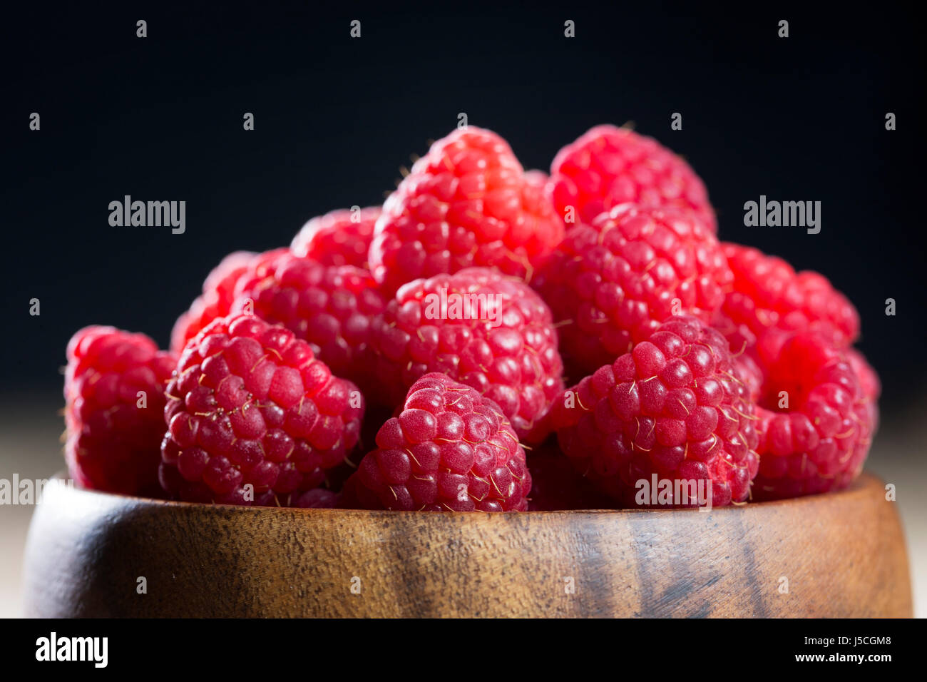 One Raspberry On A Table Clos up of a bowl of raspberries sitting on a rustic wooden table Stock ...