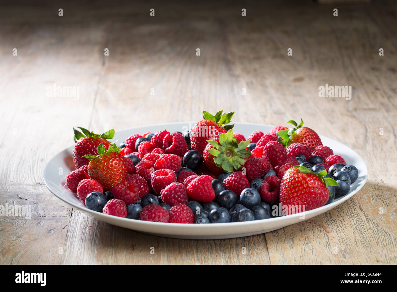 Plate of fresh berries sitting on a rustic wooden table. Stock Photo