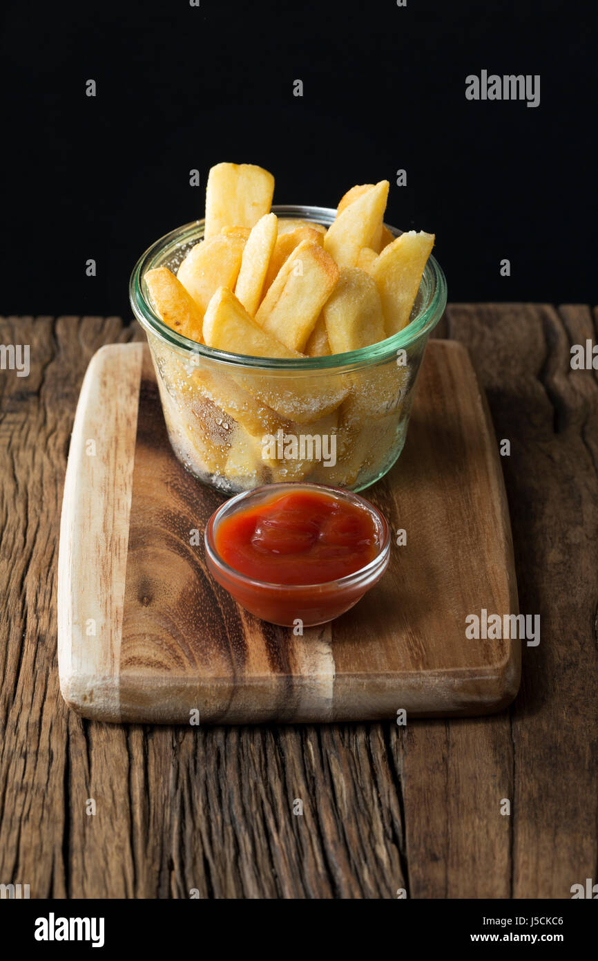 Fresh french fries or hot potato chips served in a glass bowl. The food is sitting on a rustic wooden background. Stock Photo
