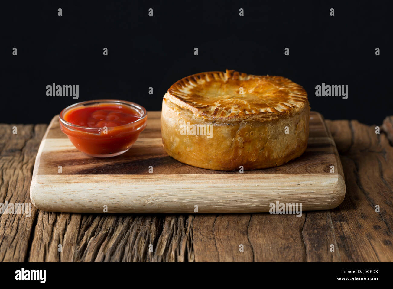 A Traditional British meat pie sitting on a rustic wooden table. Stock Photo