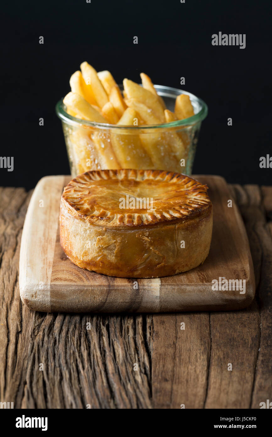 A Traditional British meat pie and chips sitting on a rustic wooden table. Stock Photo