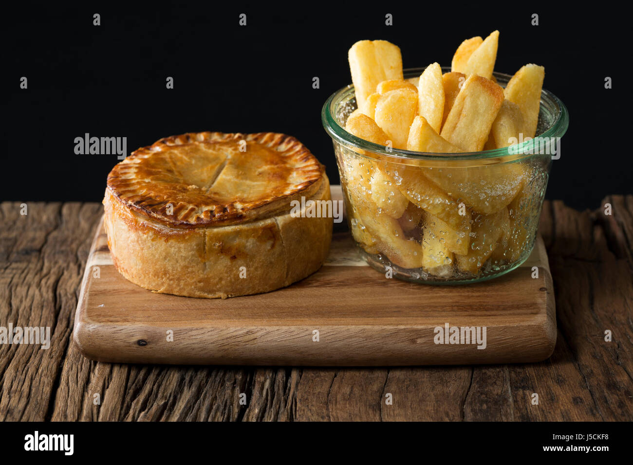A Traditional British meat pie and chips sitting on a rustic wooden