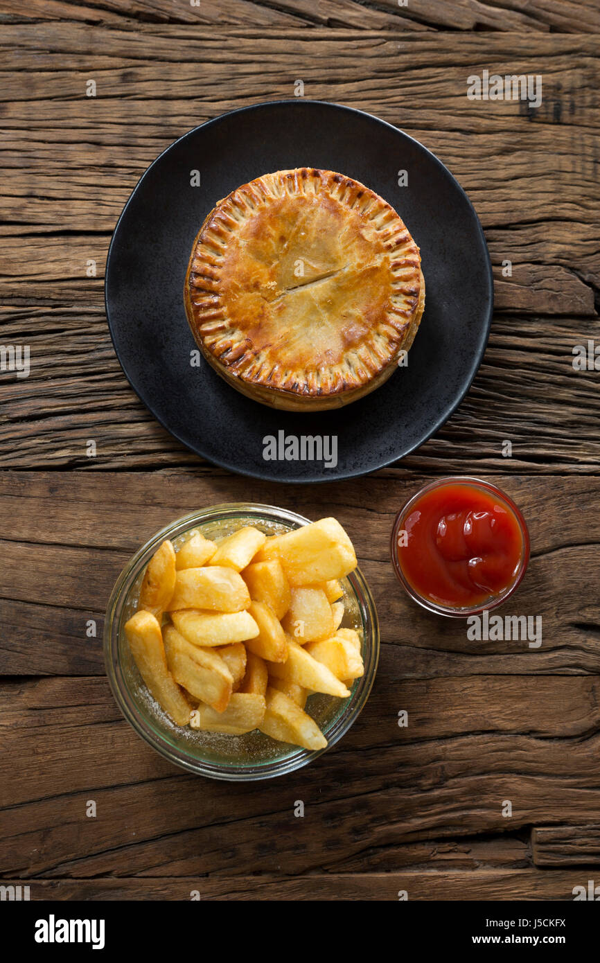 A Traditional British meat pie and chips sitting on a rustic wooden