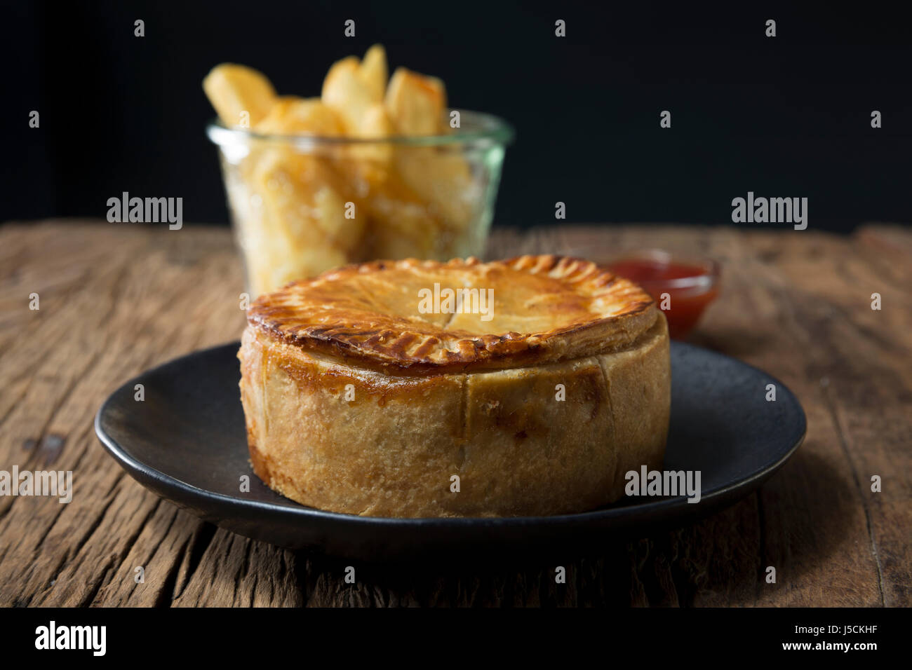 A Traditional British meat pie and chips sitting on a rustic wooden